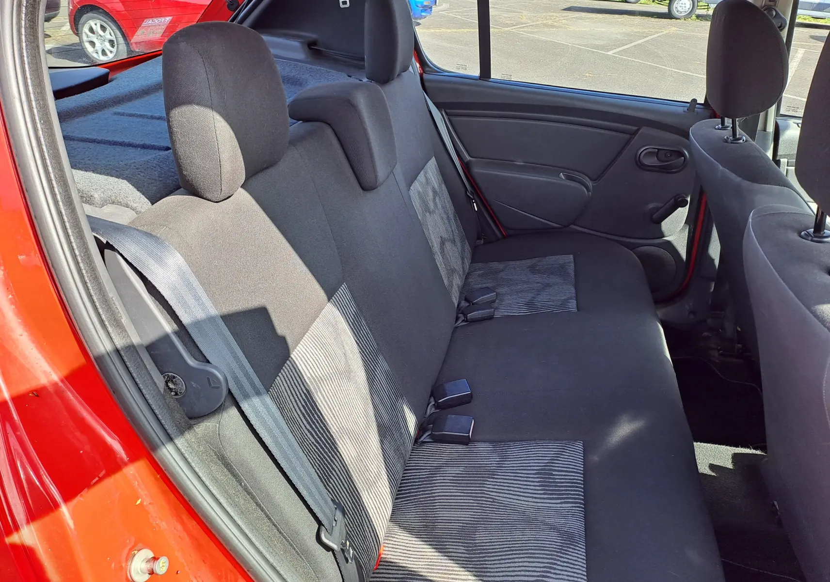 Vue intérieure côté gauche des sièges arrière en tissu noir et gris d'une Dacia Sandero rouge de 2010.