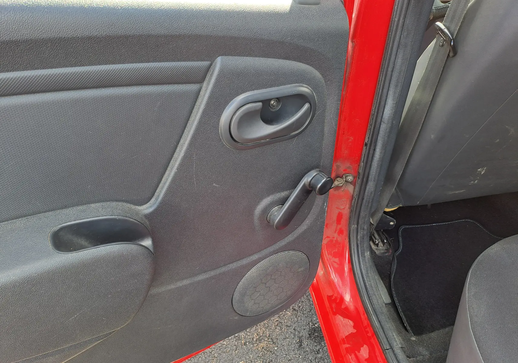 Vue intérieure de la porte arrière gauche rouge d'une Dacia Sandero 2010 avec poignée manuelle et haut-parleur intégré.