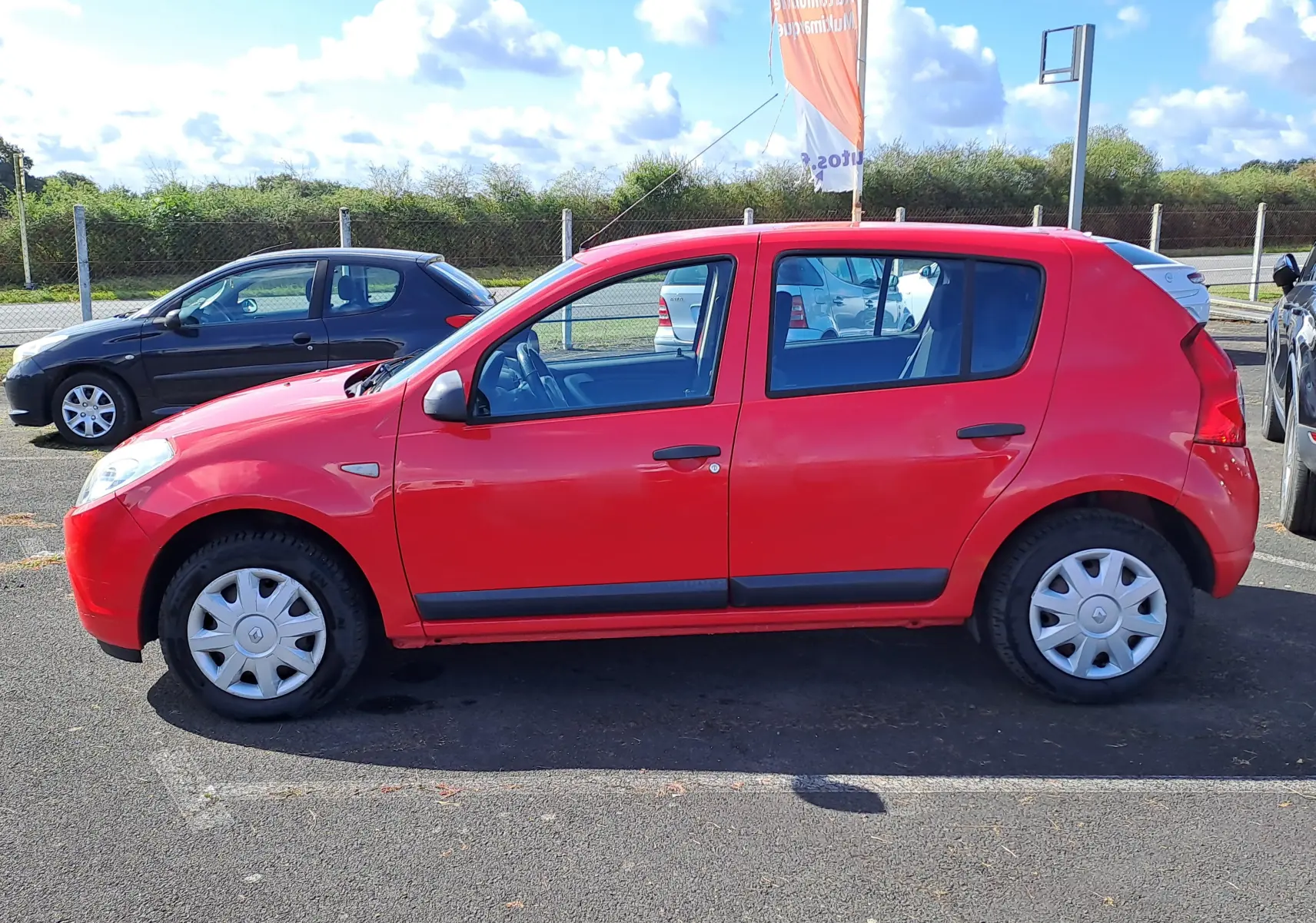 Vue latérale gauche d'une Dacia Sandero rouge de 2010, compacte avec jantes en acier et poignées noires.