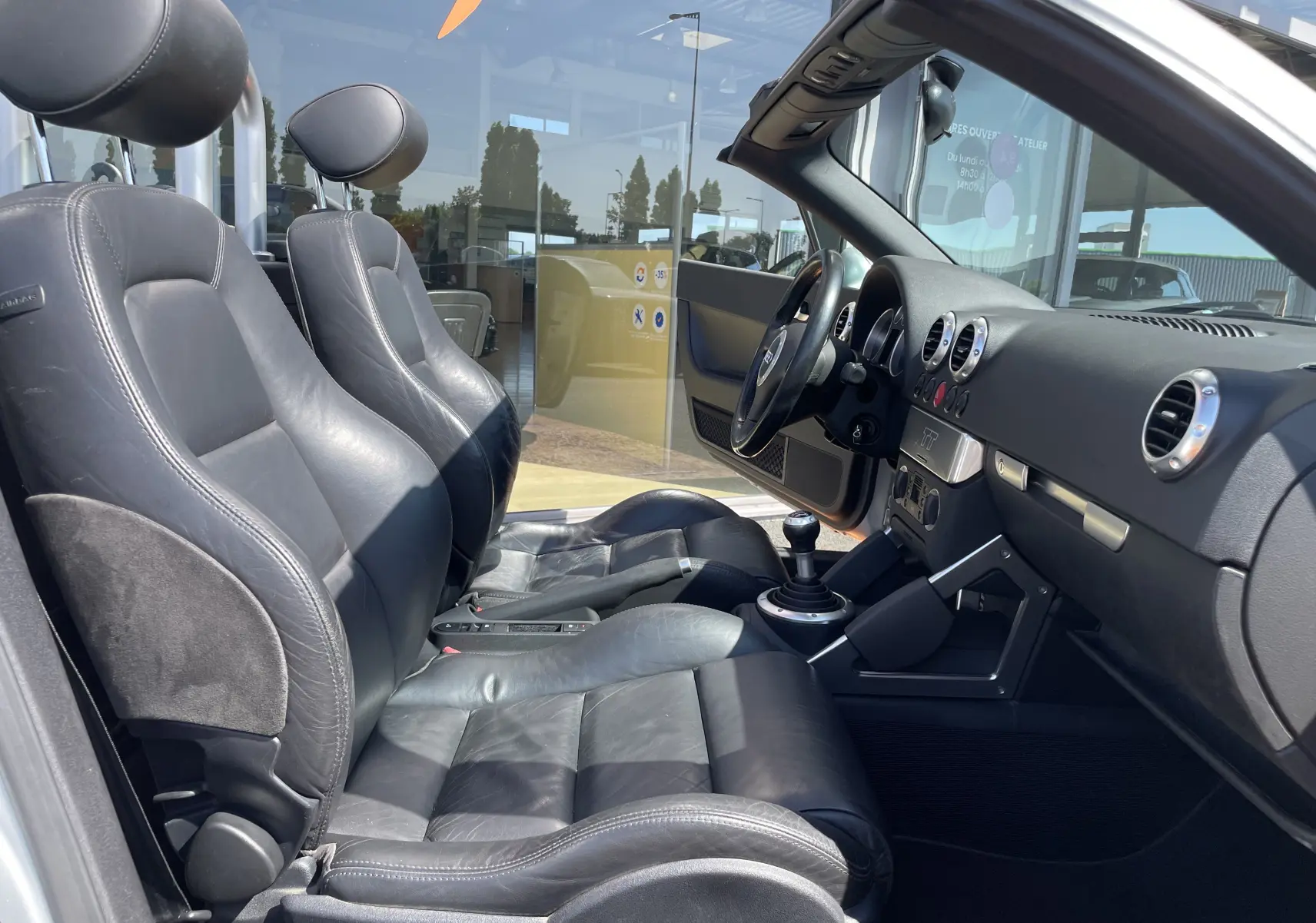 Intérieur noir cuir de l'Audi TT Roadster 1.8T 180 de 2002, vue côté conducteur avec tableau de bord et levier manuel visible.