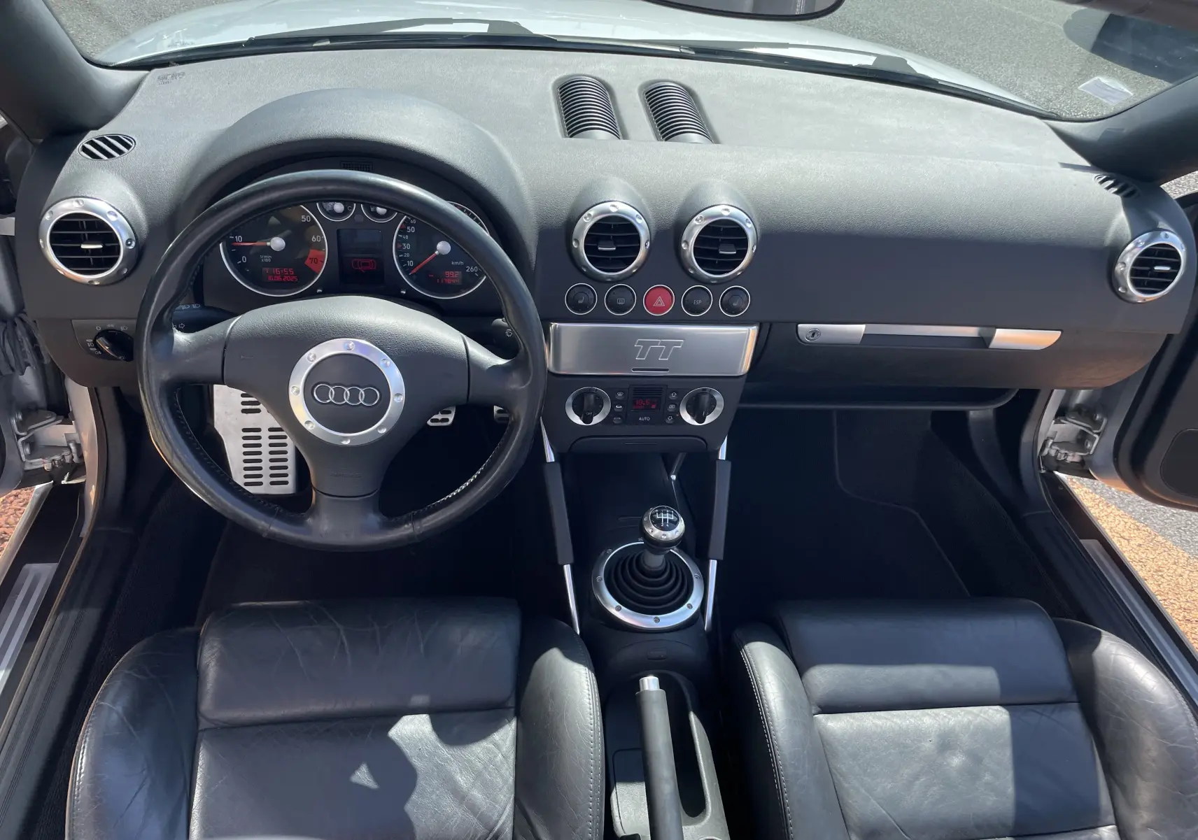 Vue intérieure frontale de l'Audi TT Roadster 1.8T 180 2002, montrant le tableau de bord noir et la boîte manuelle.