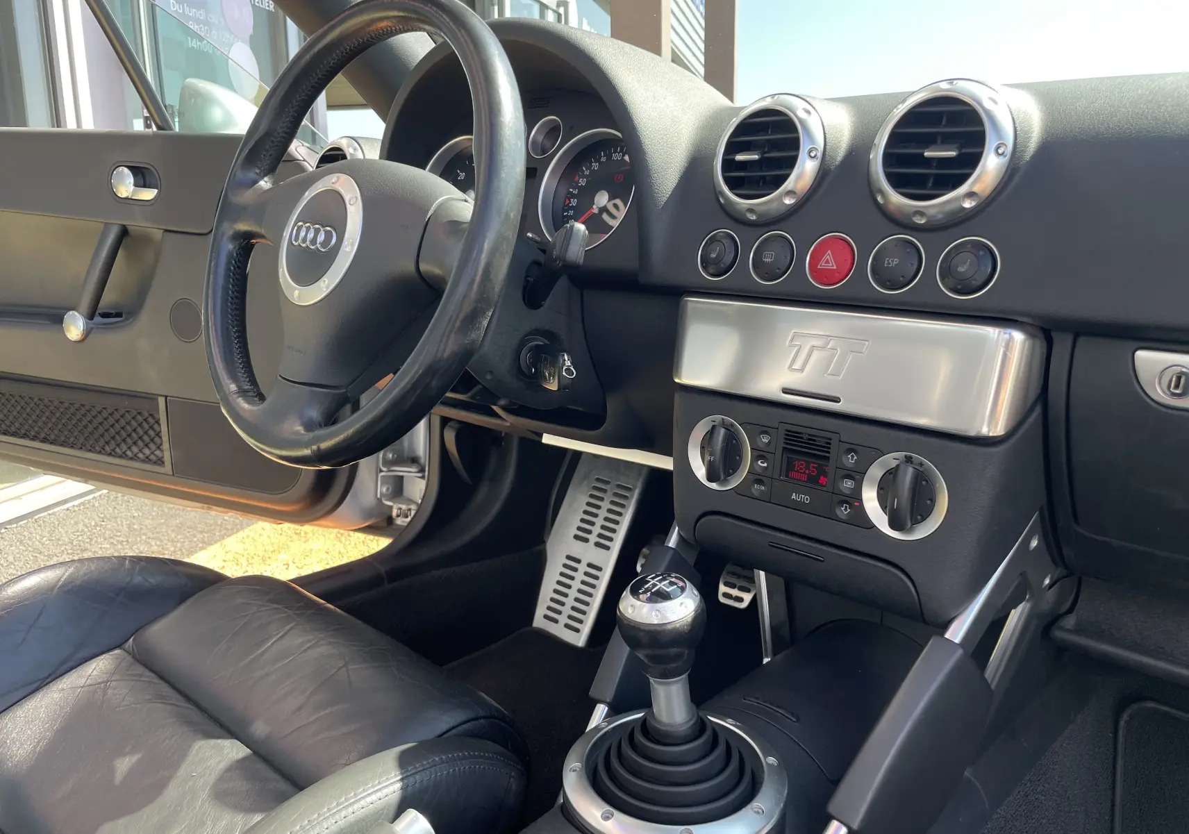 Vue intérieure côté conducteur de l'Audi TT Roadster 1.8T 180 de 2002, volant cuir noir et levier de vitesses manuel.