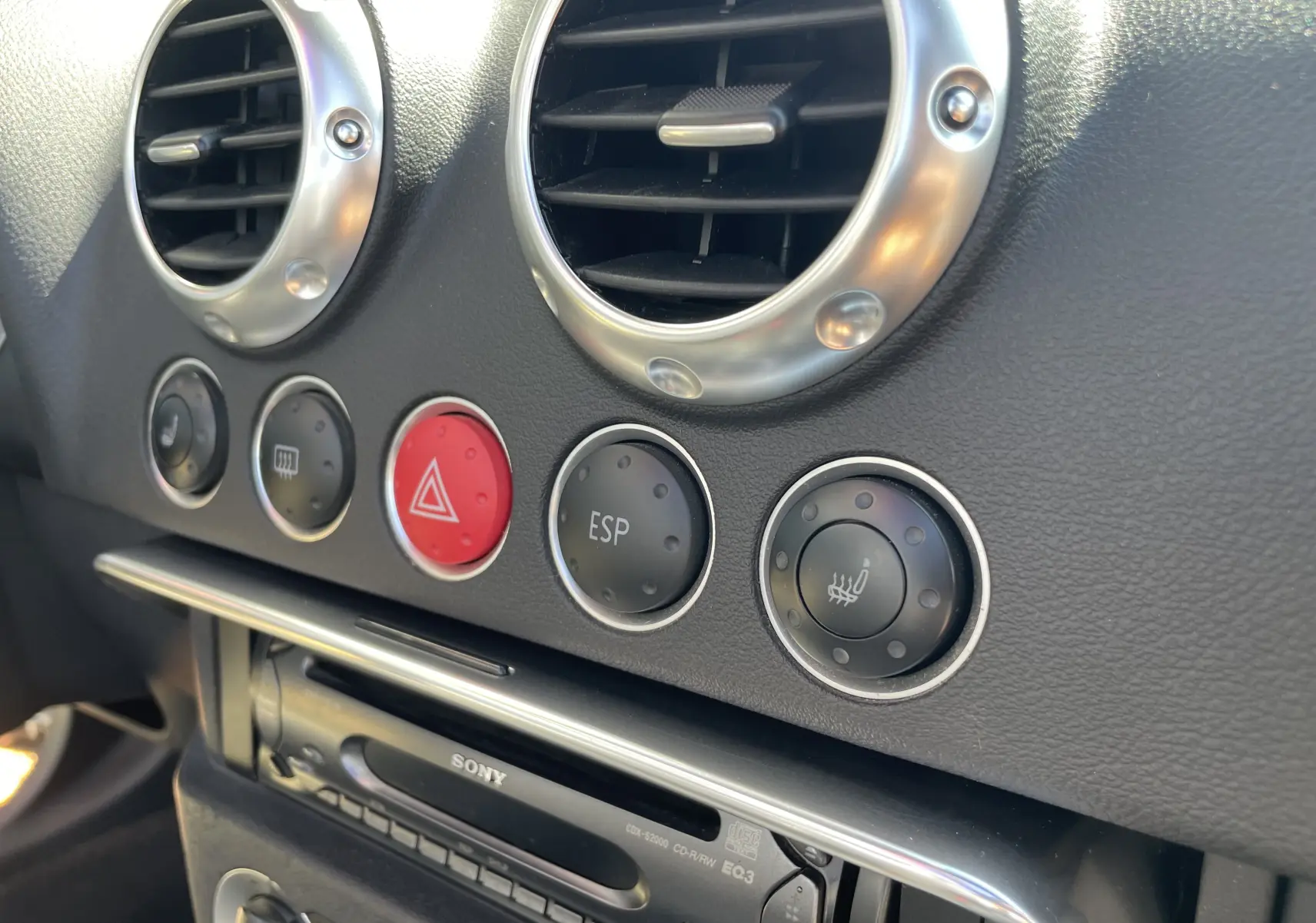 Gros plan sur la console centrale de l'Audi TT Roadster 1.8T 180 gris argent de 2002, montrant les aérateurs ronds et les boutons de contrôle.