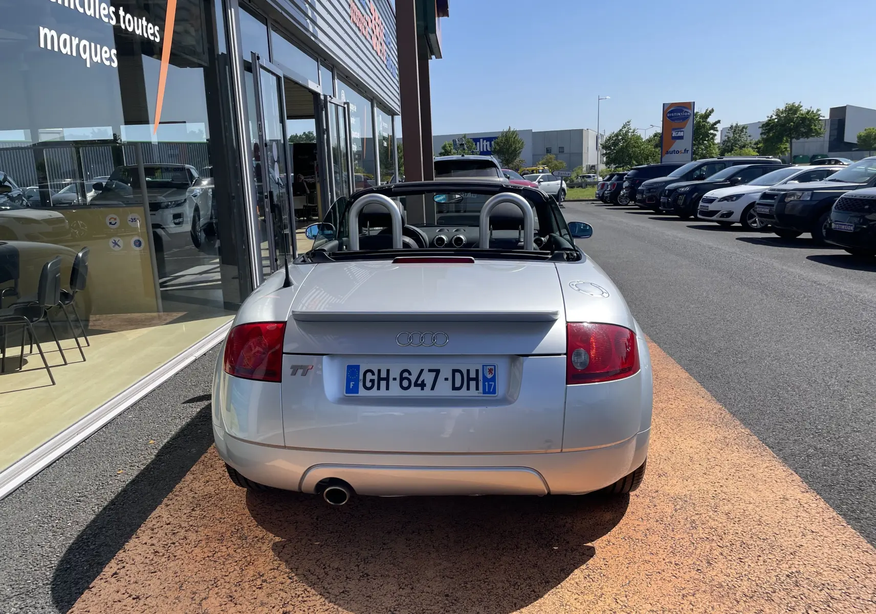 Vue arrière d'une Audi TT Roadster gris argent de 2002, capote ouverte et double arceau de sécurité visibles.