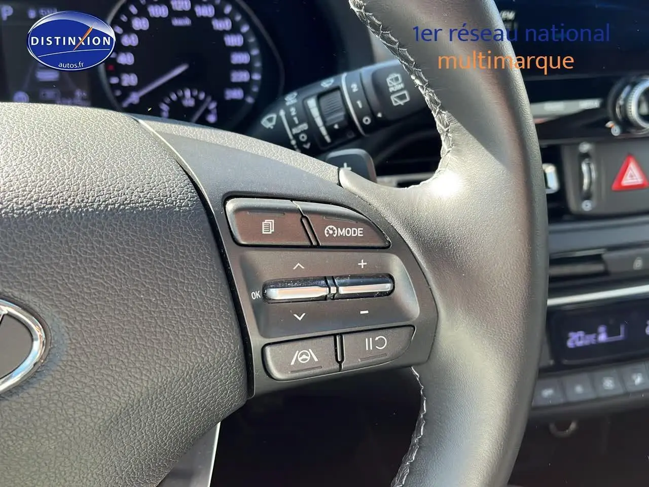 Gros plan sur le volant cuir multifonction gris d'une Hyundai i30 2024 avec commandes de régulateur et tableau de bord flou.