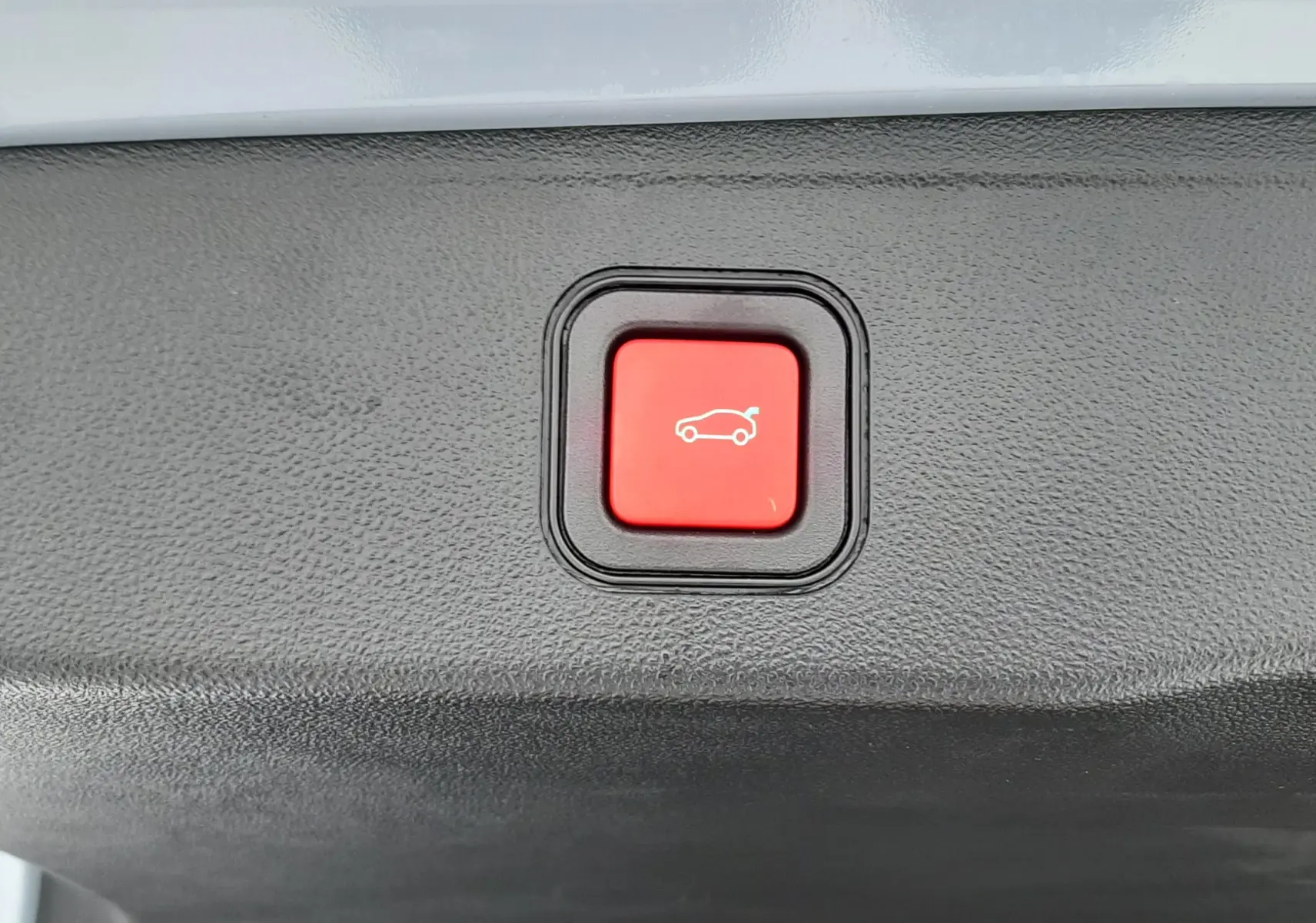 Bouton rouge d'ouverture électrique du hayon sur le coffre intérieur d'un Jeep Avenger Storm Grey 2025.