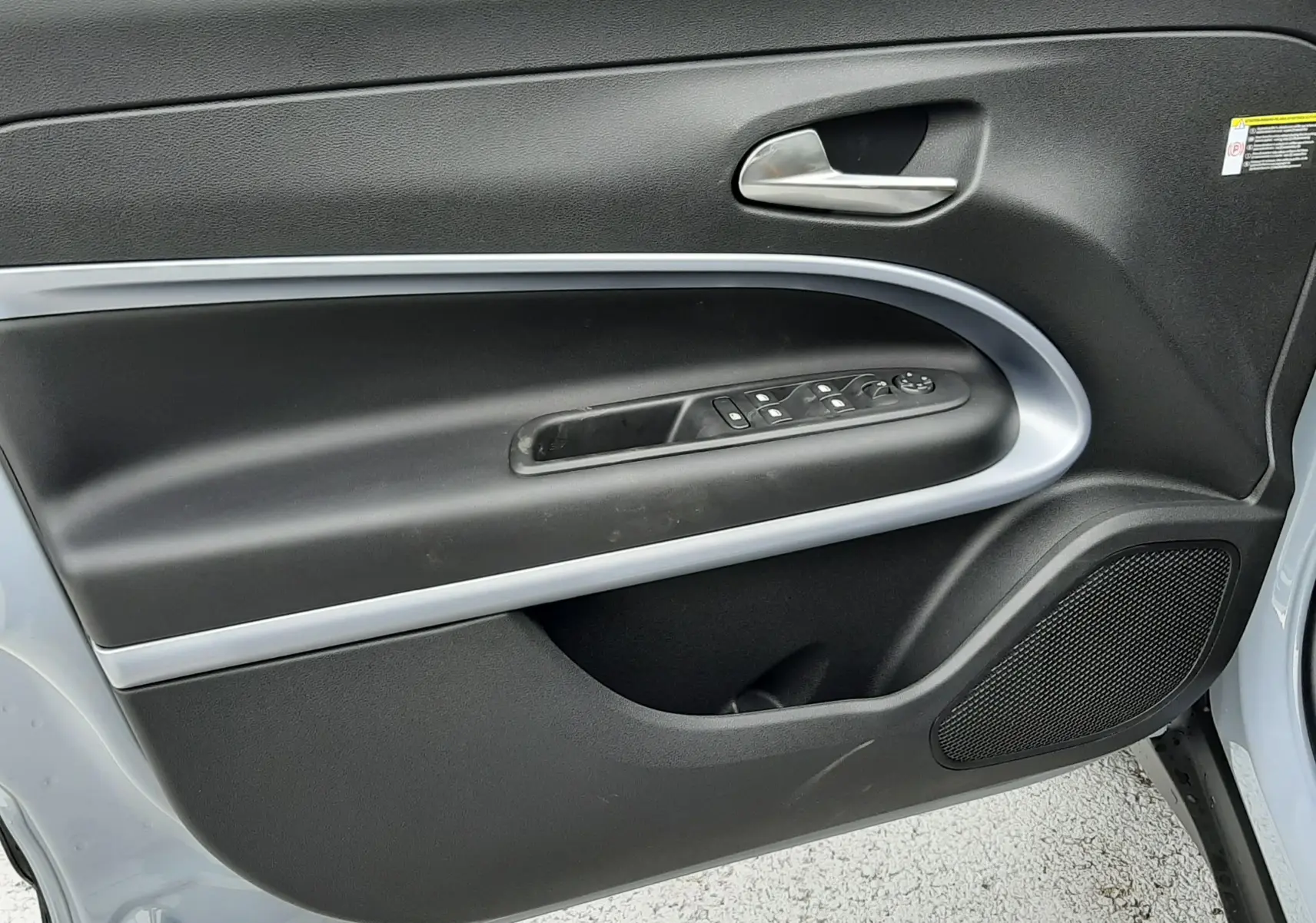 Vue intérieure côté gauche de la porte avant d’un Jeep Avenger 2025 gris Storm avec garniture noire et commandes électriques.