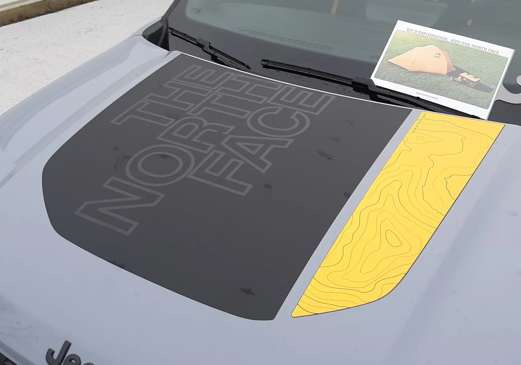 Vue rapprochée du capot avant gris Storm avec marquage noir "The North Face" et bande jaune topographique du Jeep Avenger 2025.
