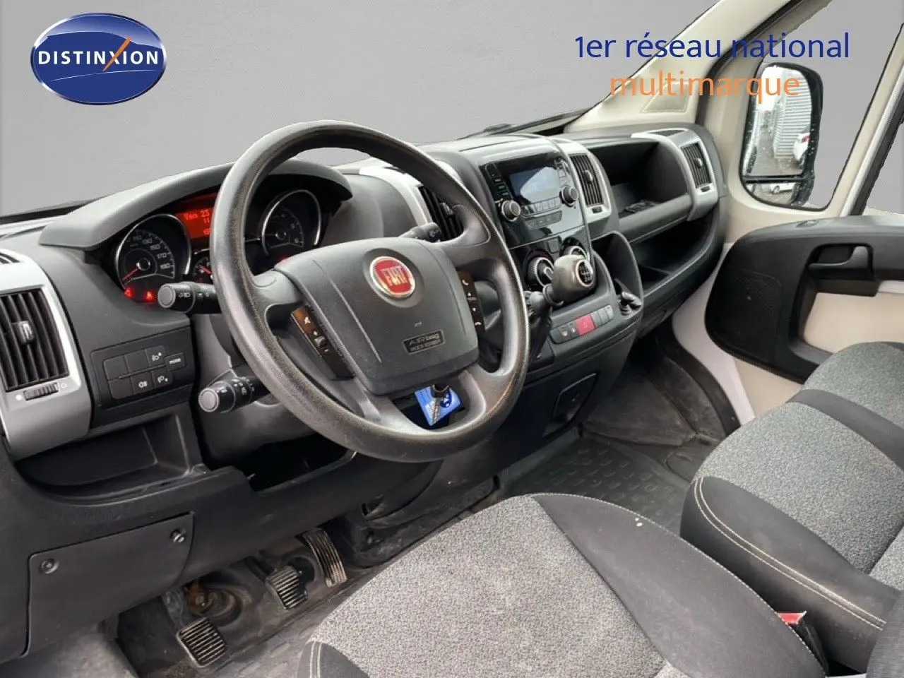 Vue intérieure côté conducteur du Fiat Ducato Fourgon 2014, montrant le volant, tableau de bord et sièges gris.