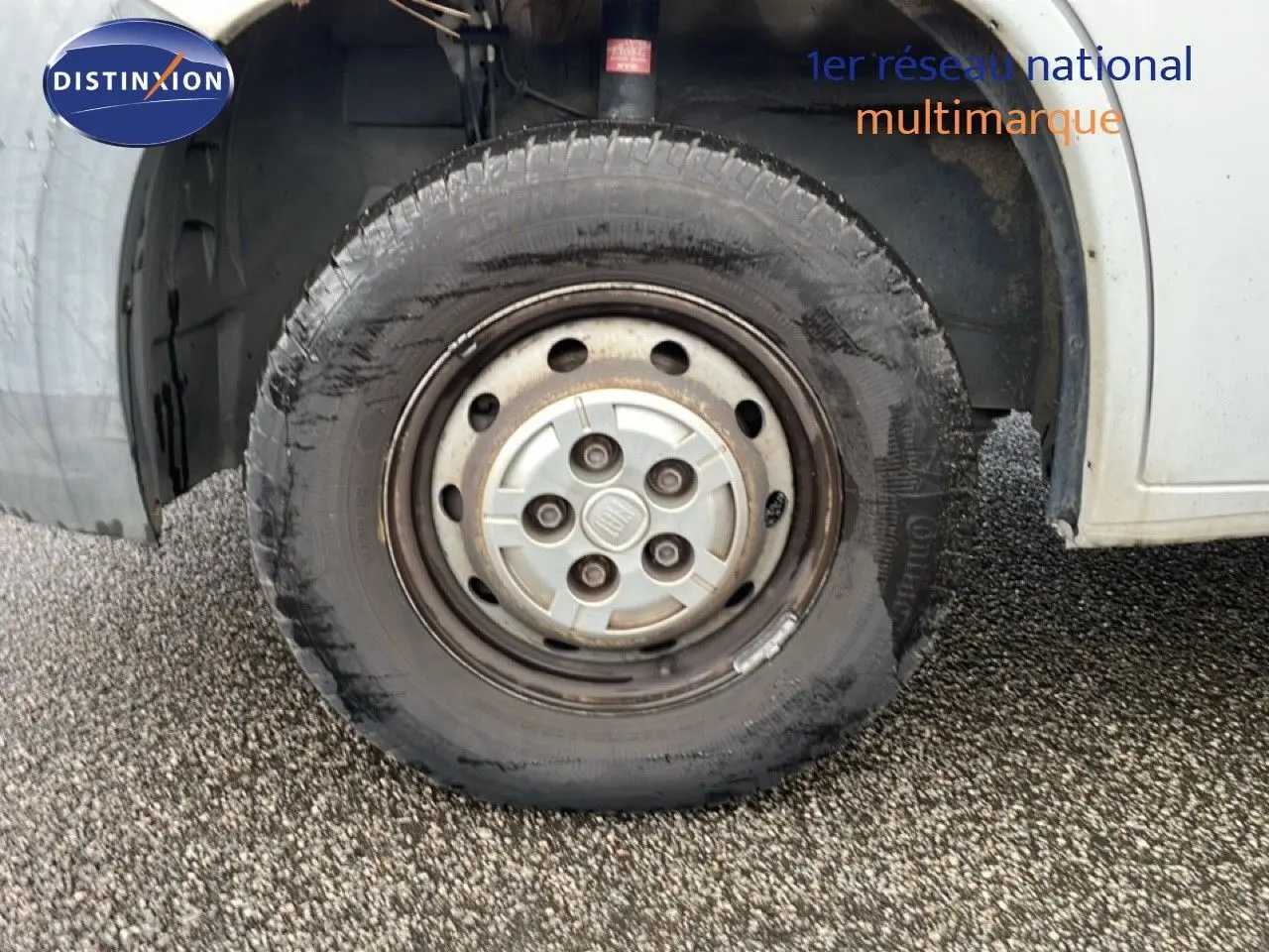 Gros plan sur la roue avant gauche blanche d’un Fiat Ducato Fourgon 2014, pneu légèrement usé sur sol gravillonné.