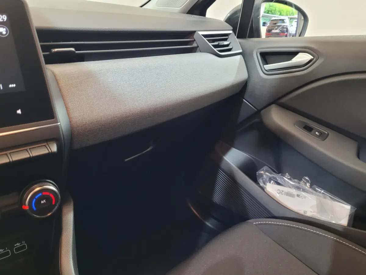 Vue intérieure côté passager de la Renault Clio gris foncé, avec tableau de bord et portière en tissu et plastique.