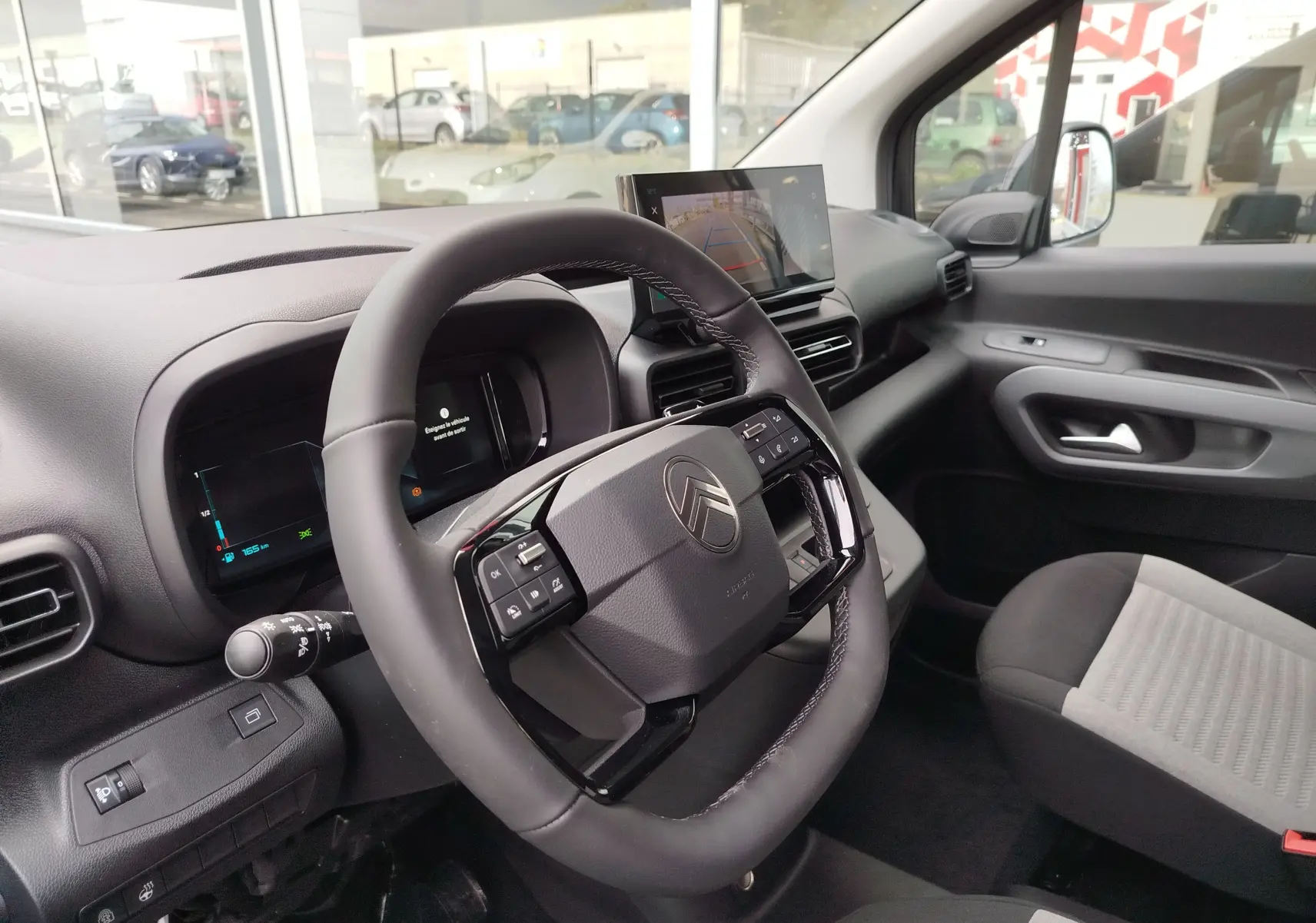 Vue intérieure côté conducteur du Citroën Berlingo 2025, tableau de bord noir avec écran central et volant multifonction.