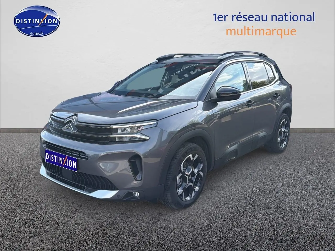 Vue 3/4 avant droit d'un Citroën C5 Aircross gris platinium avec barres de toit et jantes alu distinctives.