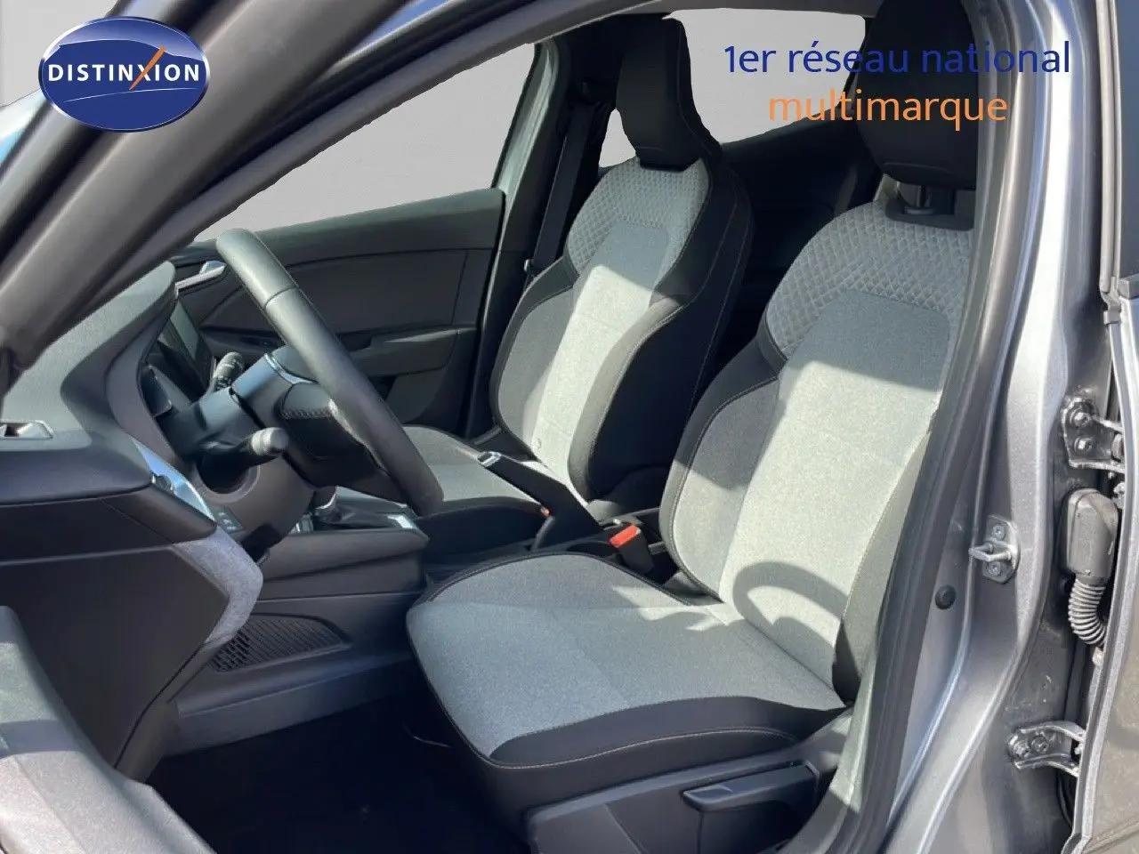 Vue intérieure côté conducteur de la Renault Clio gris schiste métal, montrant les sièges tissu bicolore et le volant multifonction.