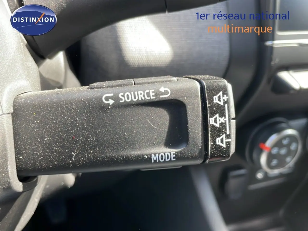 Gros plan sur la commande au volant de la Renault Clio 2025, finition gris schiste métal, avec boutons source et mode visibles.