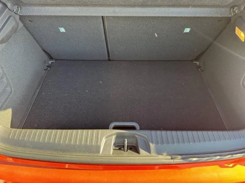 Vue plongeante sur le coffre spacieux et vide de la Renault Clio orange Valencia 2025, avec plancher plat et poignée centrale.