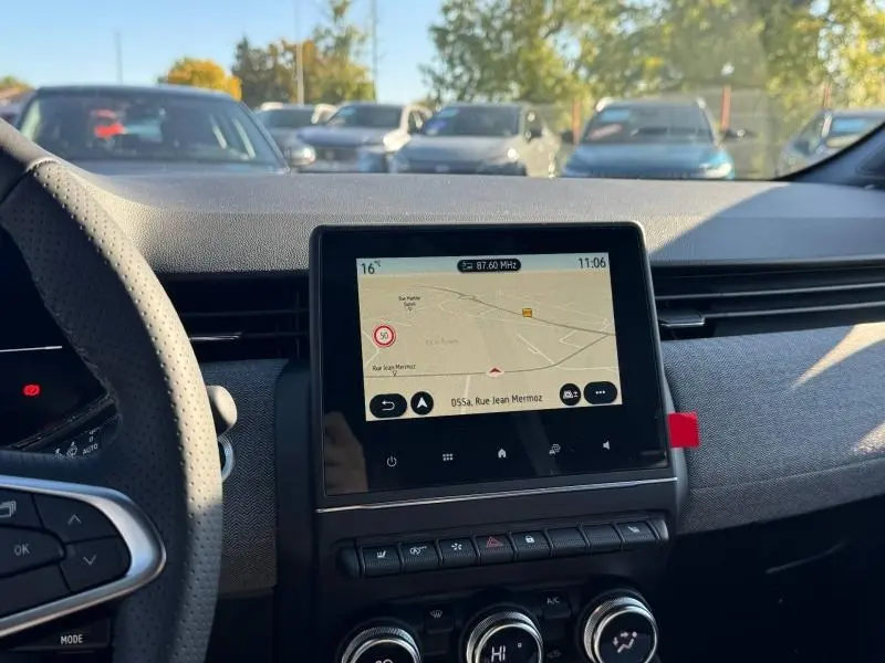 Vue intérieure centrée sur l'écran tactile du tableau de bord de la Renault Clio orange, volant partiellement visible à gauche.