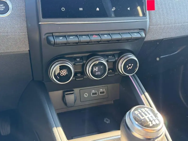 Détail intérieur du tableau de bord de la Renault Clio orange 2025, avec commandes climatisation et levier de vitesse manuel.
