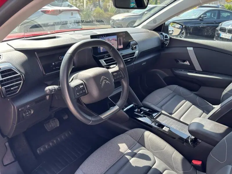 Vue intérieure côté conducteur du Citroën C4 X 2024 avec tableau de bord moderne et sièges tissu gris.