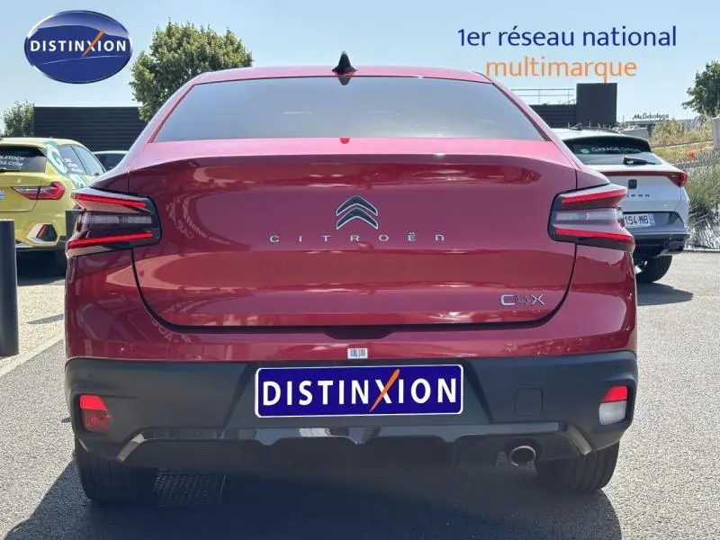 Vue arrière d'une Citroën C4 X rouge Elixir avec feux LED et logo distinctif sur un parking extérieur.