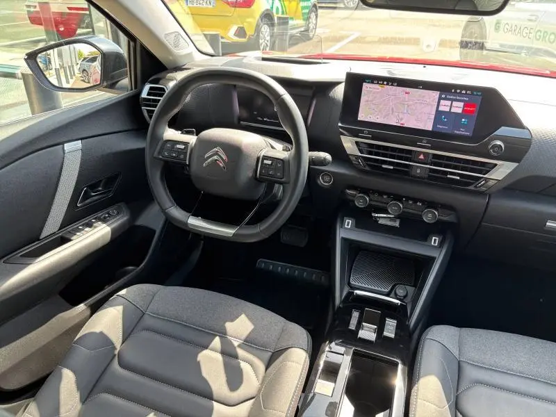 Intérieur de la Citroën C4 X 2024, vue du poste de conduite avec écran tactile et volant cuir noir.