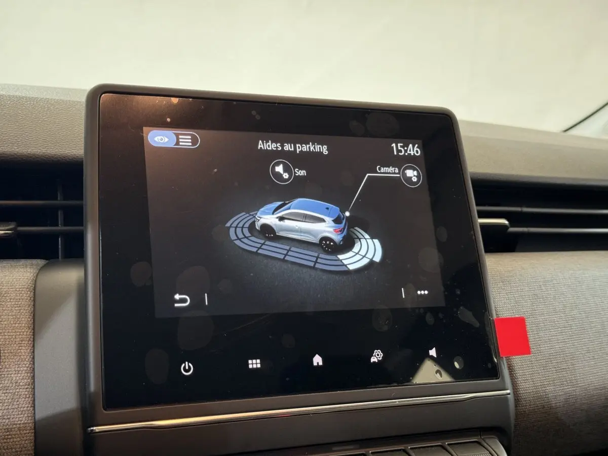 Écran tactile central montrant l'aide au stationnement d'une Renault Clio gris clair, vue intérieure rapprochée.