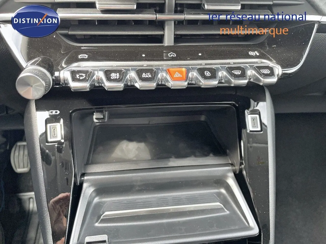 Vue rapprochée de la console centrale noire brillante avec commandes et compartiment ouvert d'une Peugeot 208 jaune Agueda Metal.