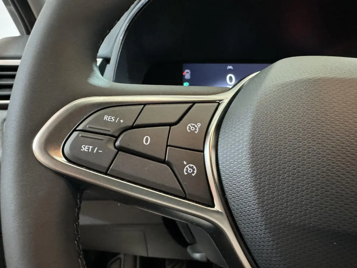 Gros plan sur le volant cuir synthétique de la Renault Clio gris clair, avec commandes multifonctions et régulateur de vitesse.