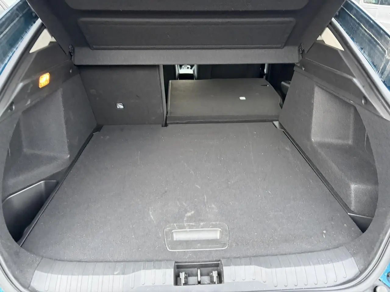 Coffre ouvert du Renault Arkana Bleu Zanzibar, vue plongeante montrant la banquette arrière partiellement rabattue.