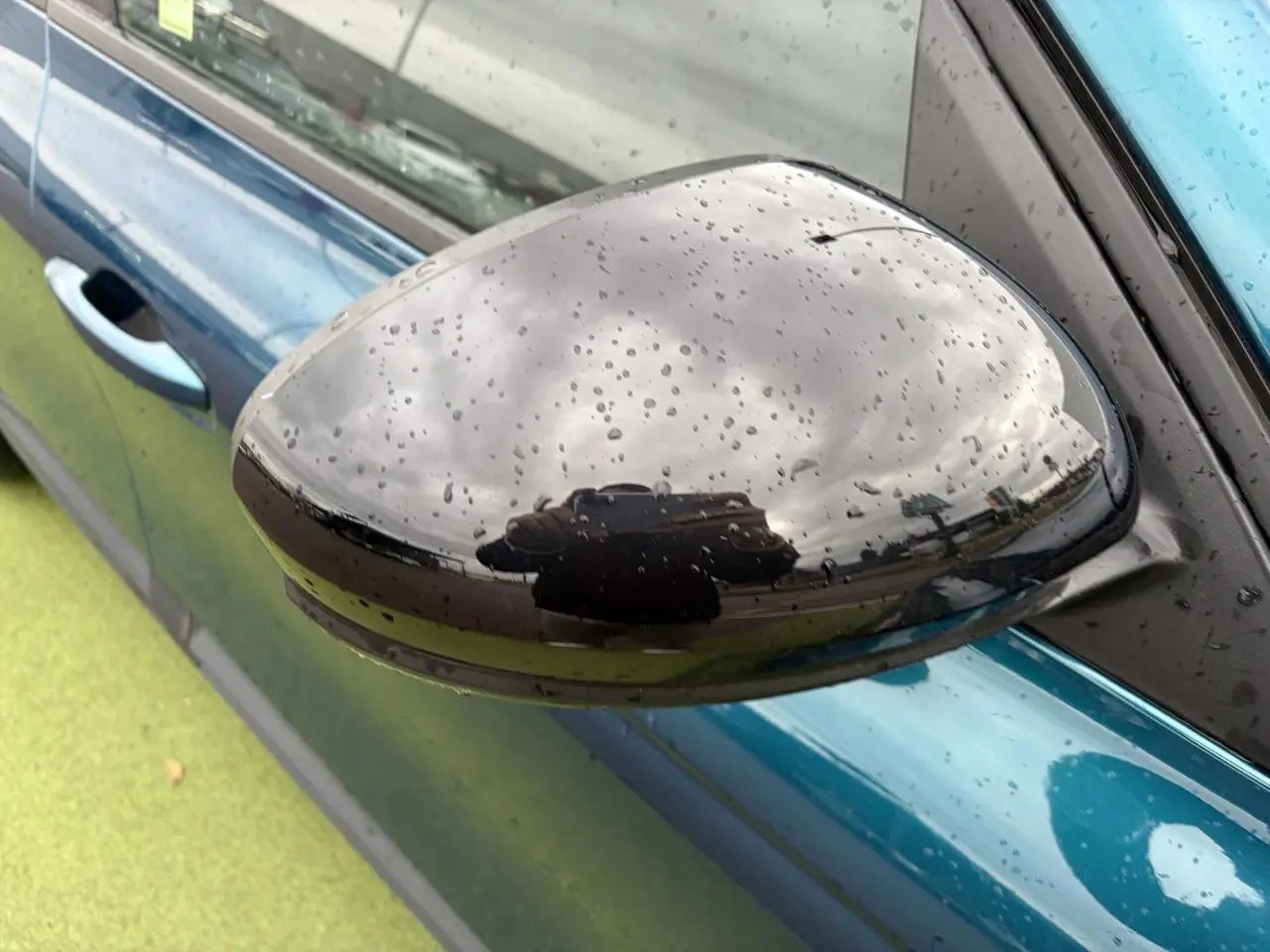 Gros plan sur le rétroviseur noir brillant côté gauche du Renault Arkana bleu Zanzibar métallisé sous la pluie.