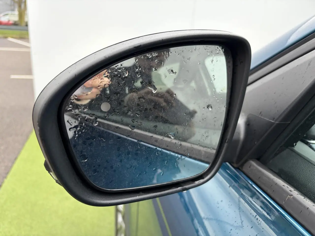 Rétroviseur droit d’un Renault Arkana bleu Zanzibar métal avec gouttes de pluie sur le miroir, vue rapprochée.