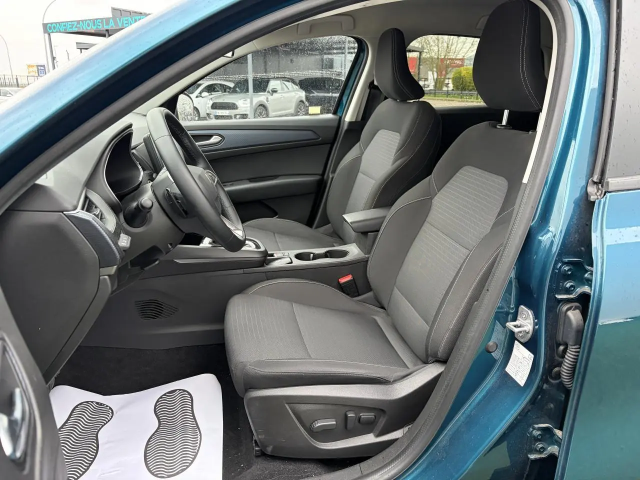 Vue intérieure côté conducteur du Renault Arkana bleu Zanzibar, sièges gris avec réglages électriques visibles.