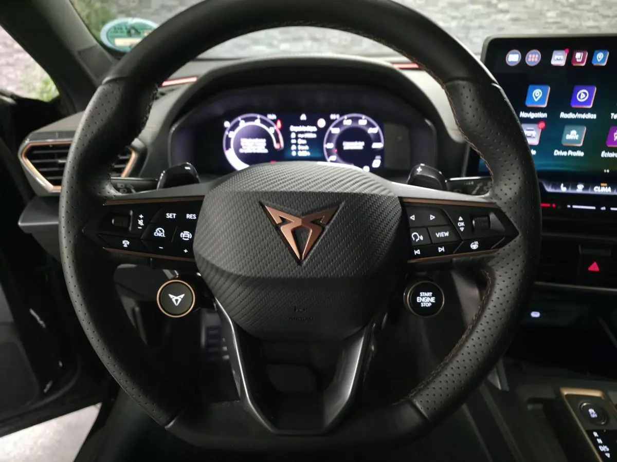 Vue rapprochée du volant noir perforé de la CUPRA Formentor avec logo cuivré et tableau de bord digital allumé.