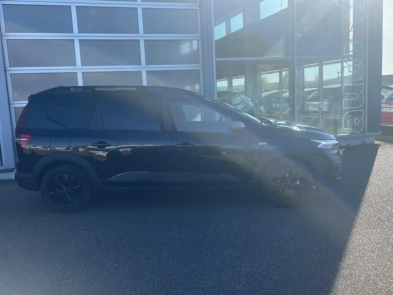 Profil côté gauche du Dacia Jogger noir nacré 2024, avec barres de toit et jantes alu noires visibles.