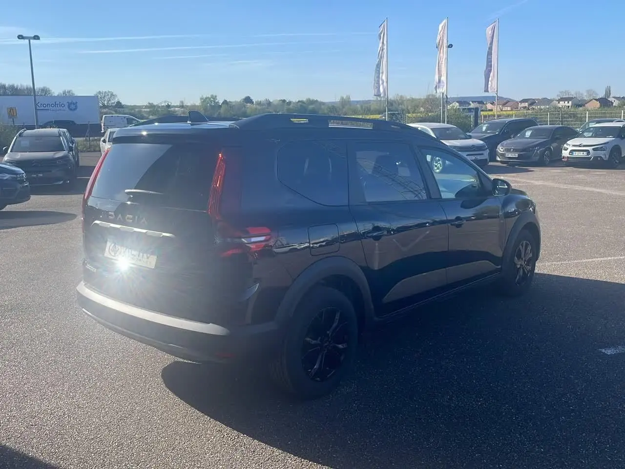 Vue 3/4 arrière droite d'un Dacia Jogger noir nacré avec barres de toit et jantes noires sur parking.