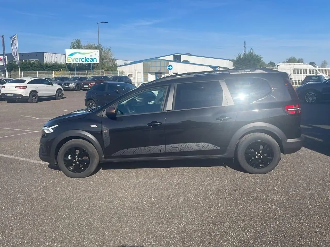 Dacia Jogger 2024 noir nacré vu de profil côté gauche, avec barres de toit et jantes noires.