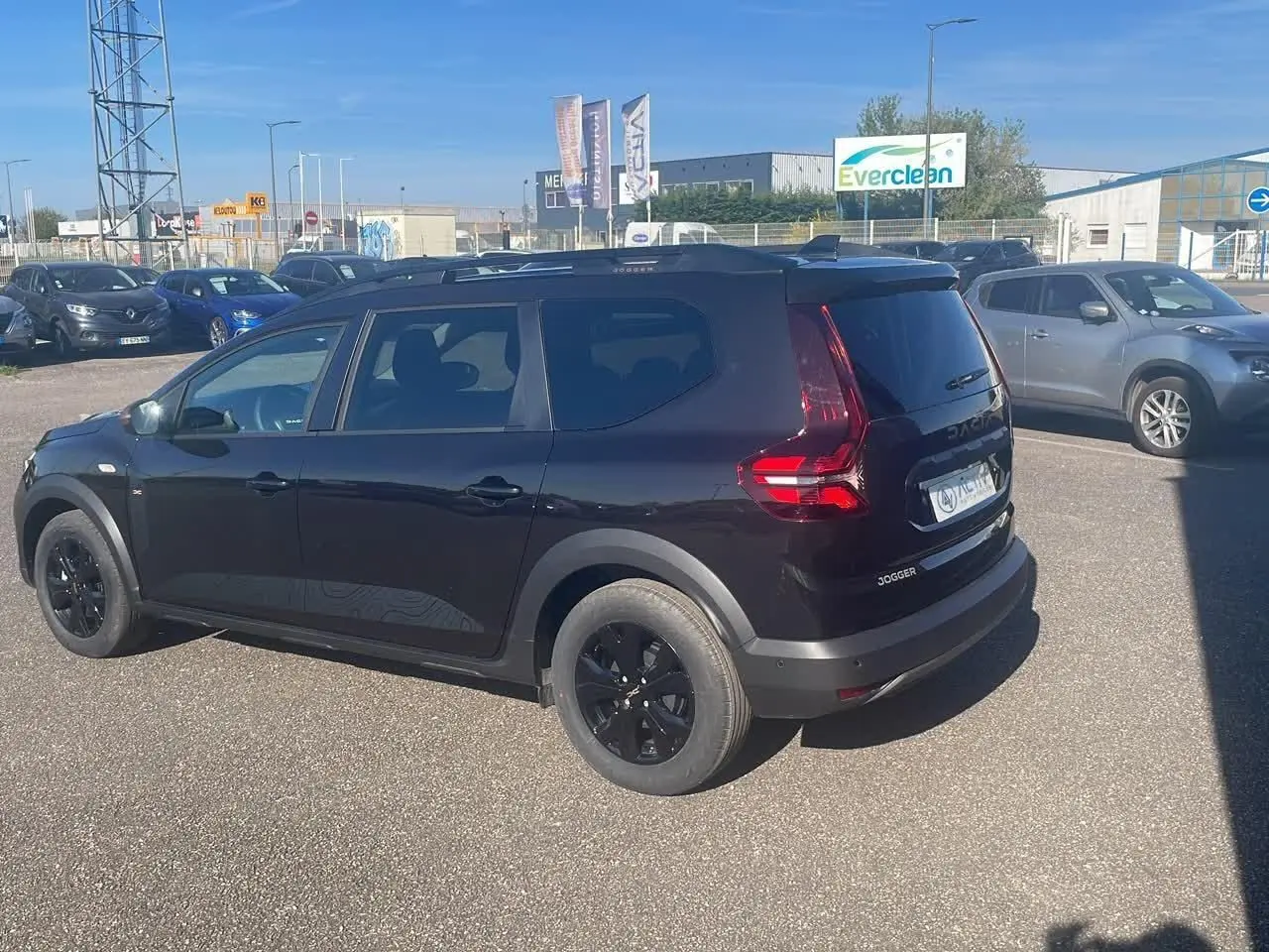 Dacia Jogger noir nacré vue 3/4 arrière droit, avec jantes noires et barres de toit visibles.