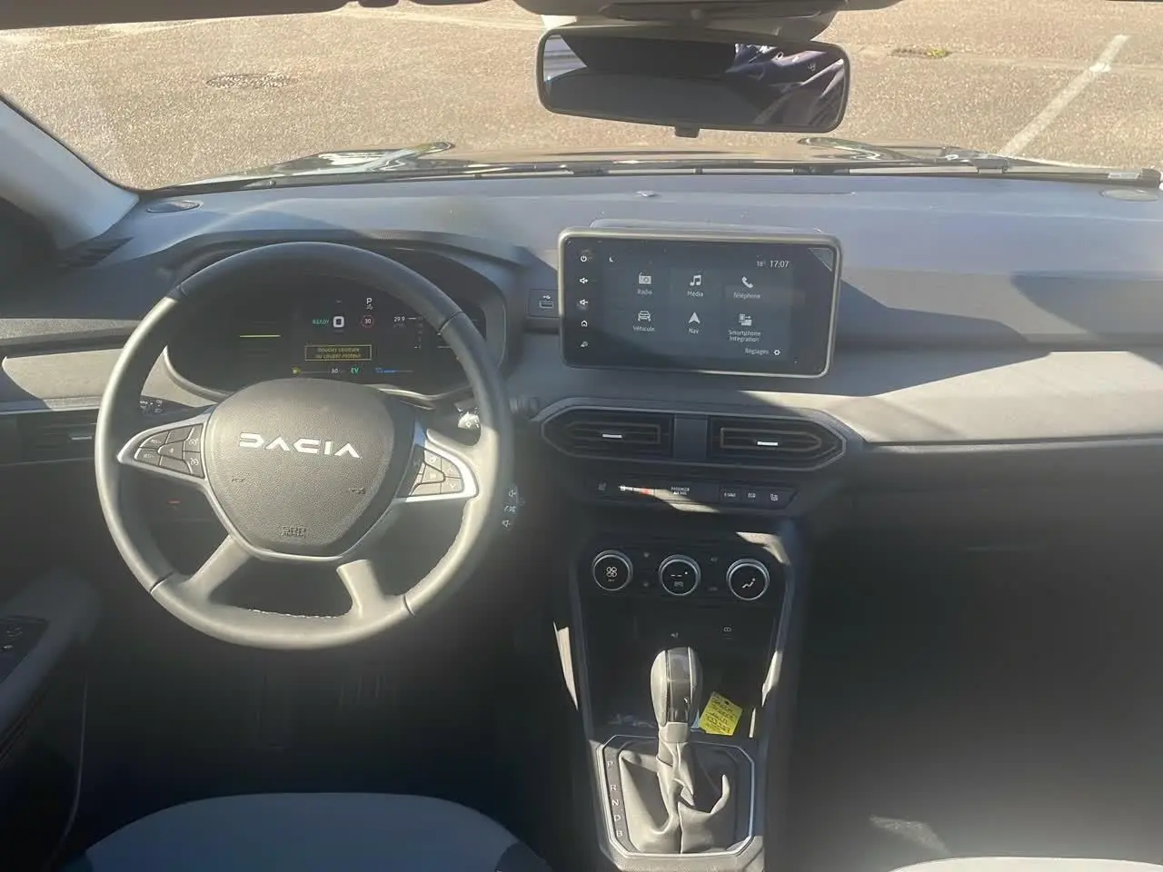 Vue frontale de l'habitacle du Dacia Jogger 2024 avec volant, écran tactile et levier de boîte automatique.