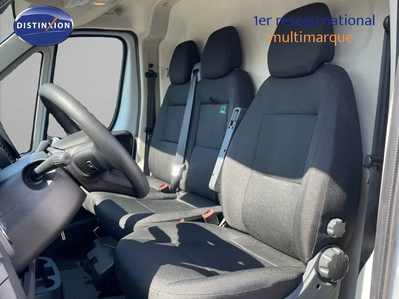 Vue intérieure côté conducteur du Peugeot Boxer Fourgon blanc banquise, montrant les sièges noirs et le volant.