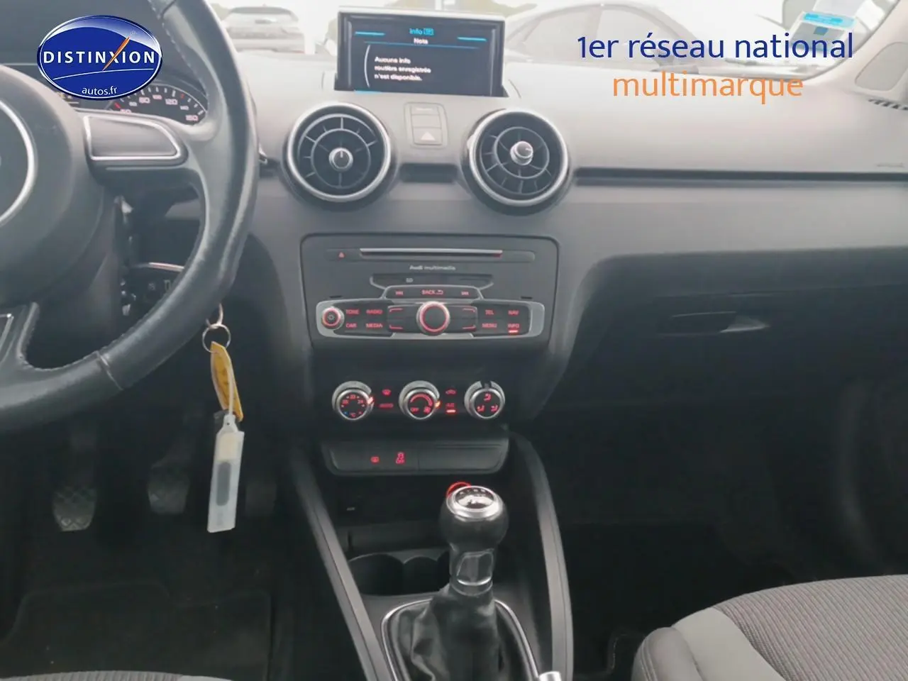 Vue intérieure centrée sur le tableau de bord et la console centrale d'une Audi A1 blanche avec boîte manuelle.