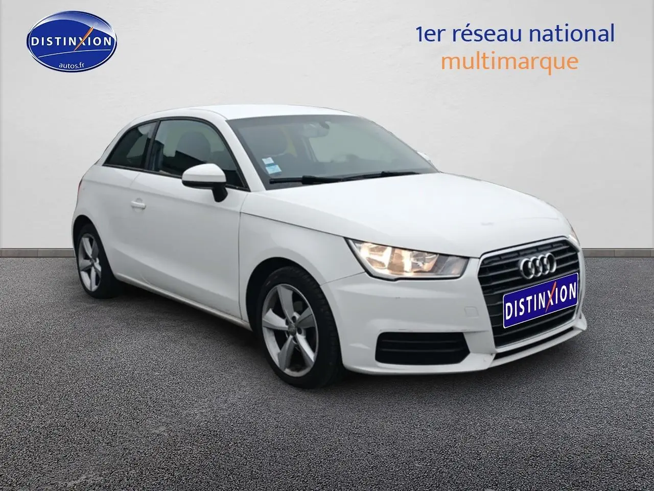 Audi A1 blanc en 3/4 avant droit avec jantes alu et phares allumés sur fond neutre.