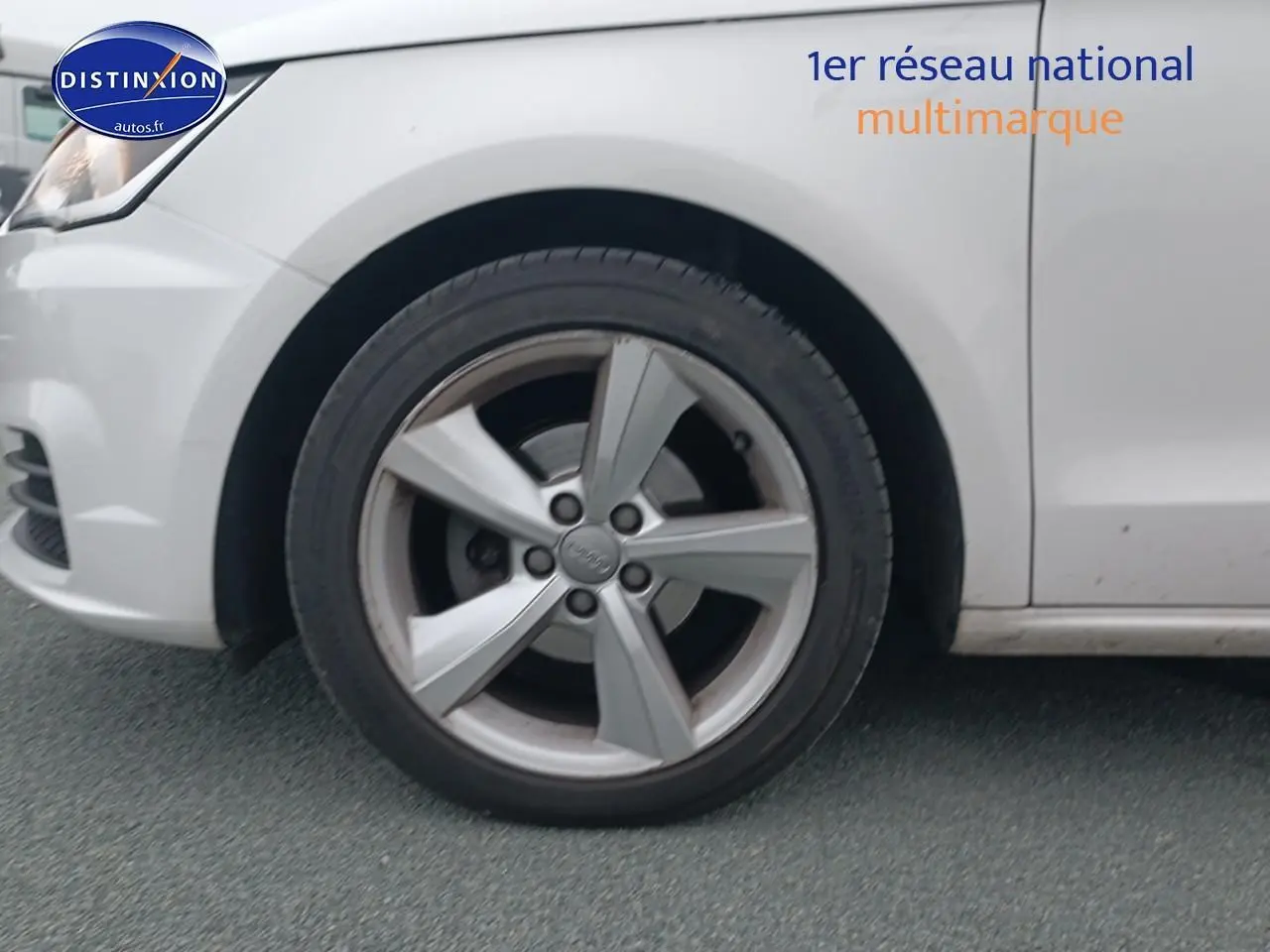 Gros plan sur la roue avant gauche d'une Audi A1 blanche, jante alliage cinq branches visible.