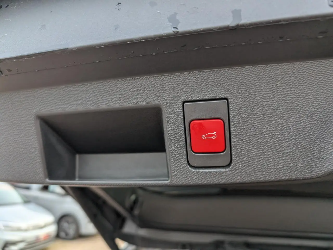 Bouton rouge d'ouverture électrique du hayon sur le panneau intérieur du coffre d'un Citroën C5 Aircross gris.