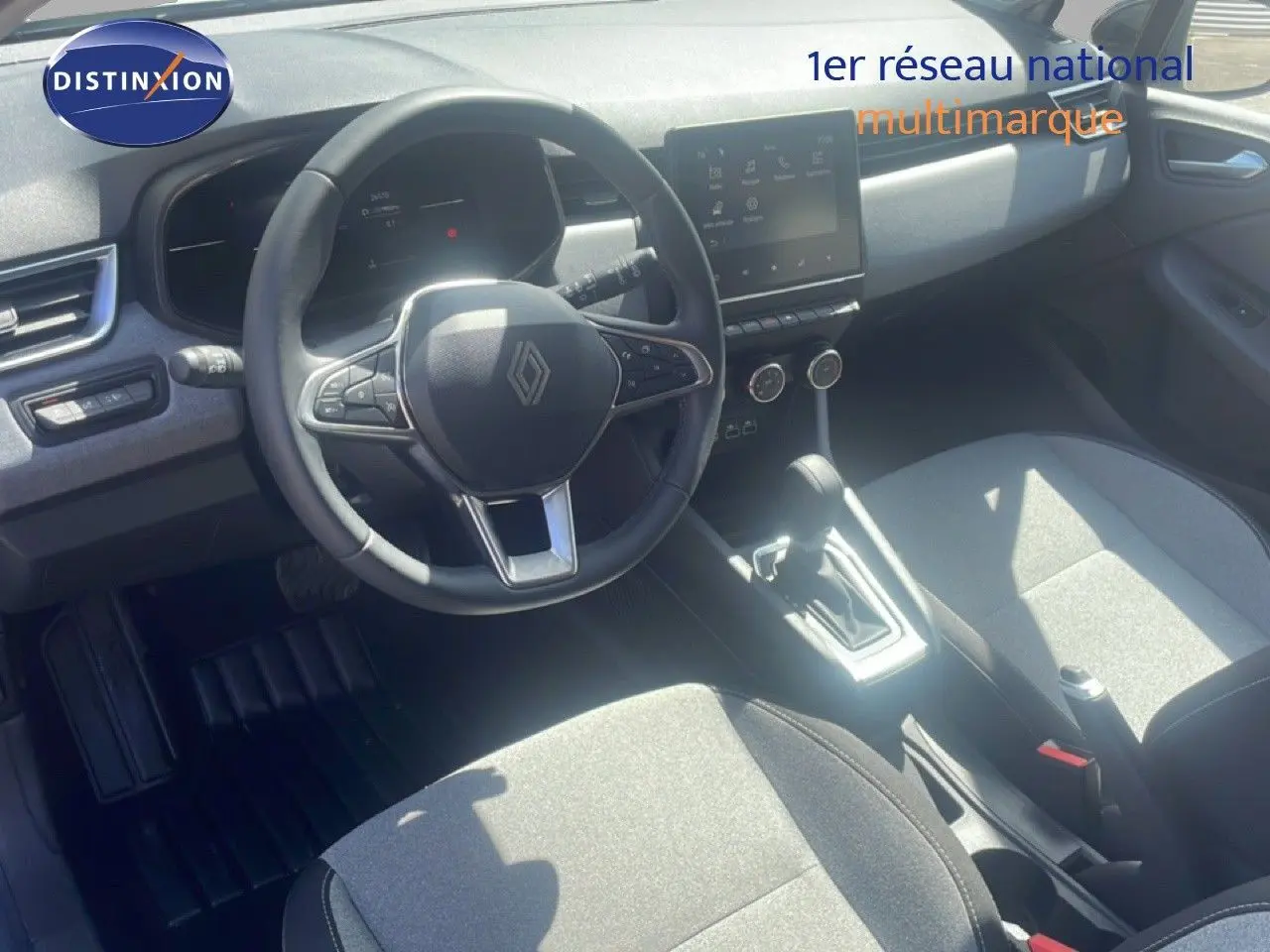 Vue intérieure de face du poste de conduite de la Renault Clio blanche 2025, avec volant multifonction et écran tactile central.
