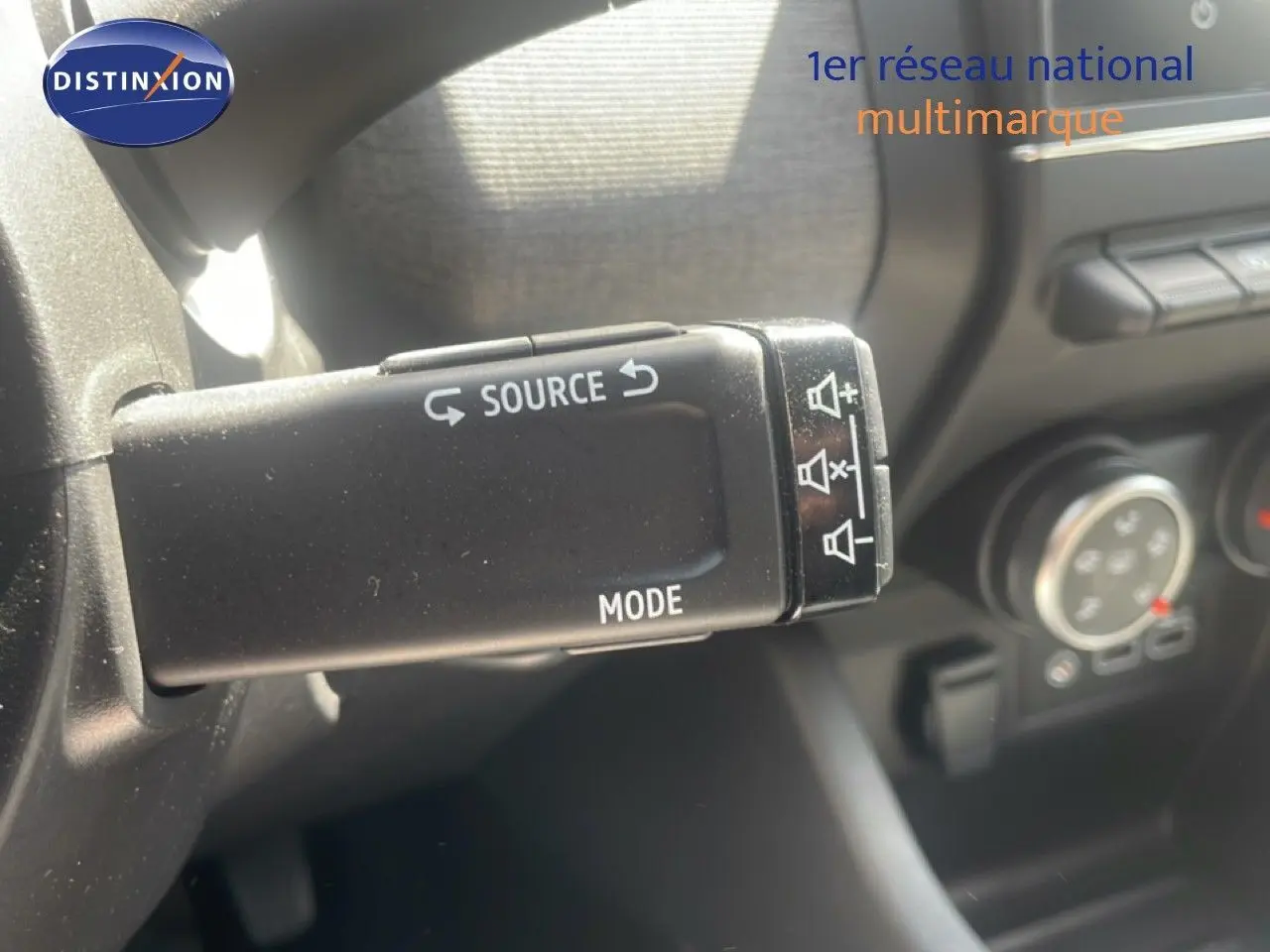 Gros plan sur la commande au volant de la Renault Clio 2025, bouton source et mode visibles dans l'habitacle noir.