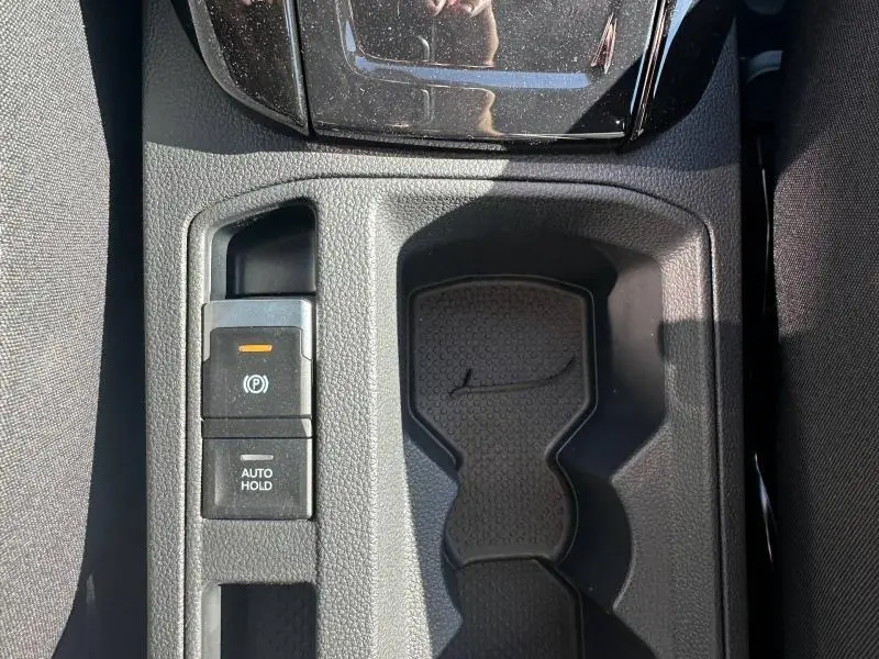Vue plongeante sur la console centrale noire du Volkswagen T-Roc 1.5 TSI Evo2 R-Line avec frein à main électronique et porte-gobelets.