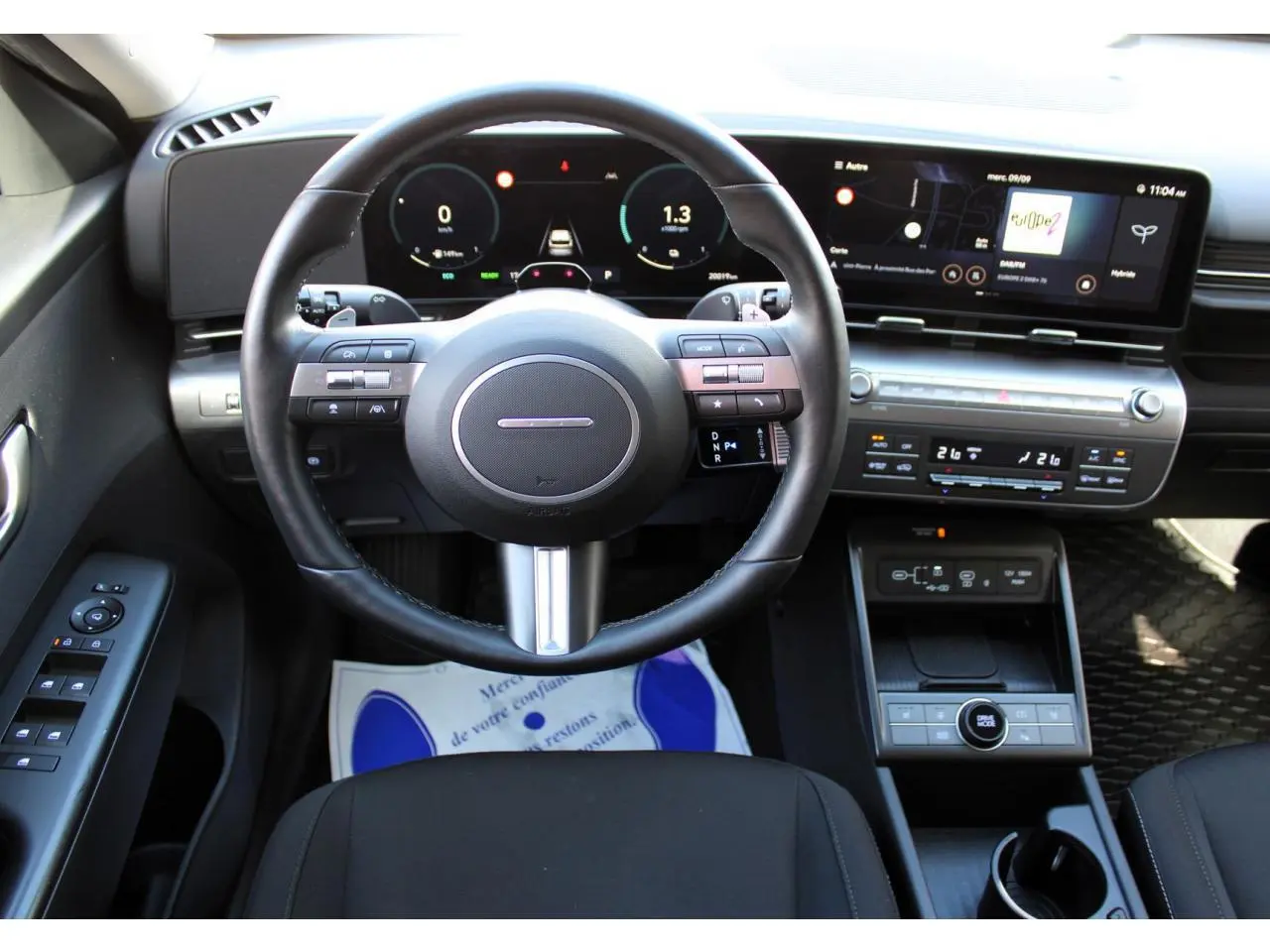 Vue intérieure frontale du tableau de bord et volant cuir du Hyundai Kona 2024 avec écran tactile panoramique.