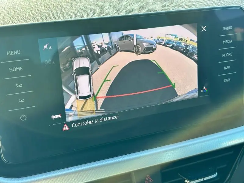 Affichage de la caméra de recul du Skoda Kamiq blanc montrant l'arrière avec lignes de guidage colorées et véhicule en stationnement.