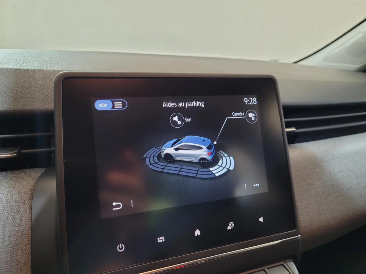Écran tactile central montrant l'aide au stationnement avec vue 3D du véhicule gris côté droit, intérieur Renault Clio 2025.