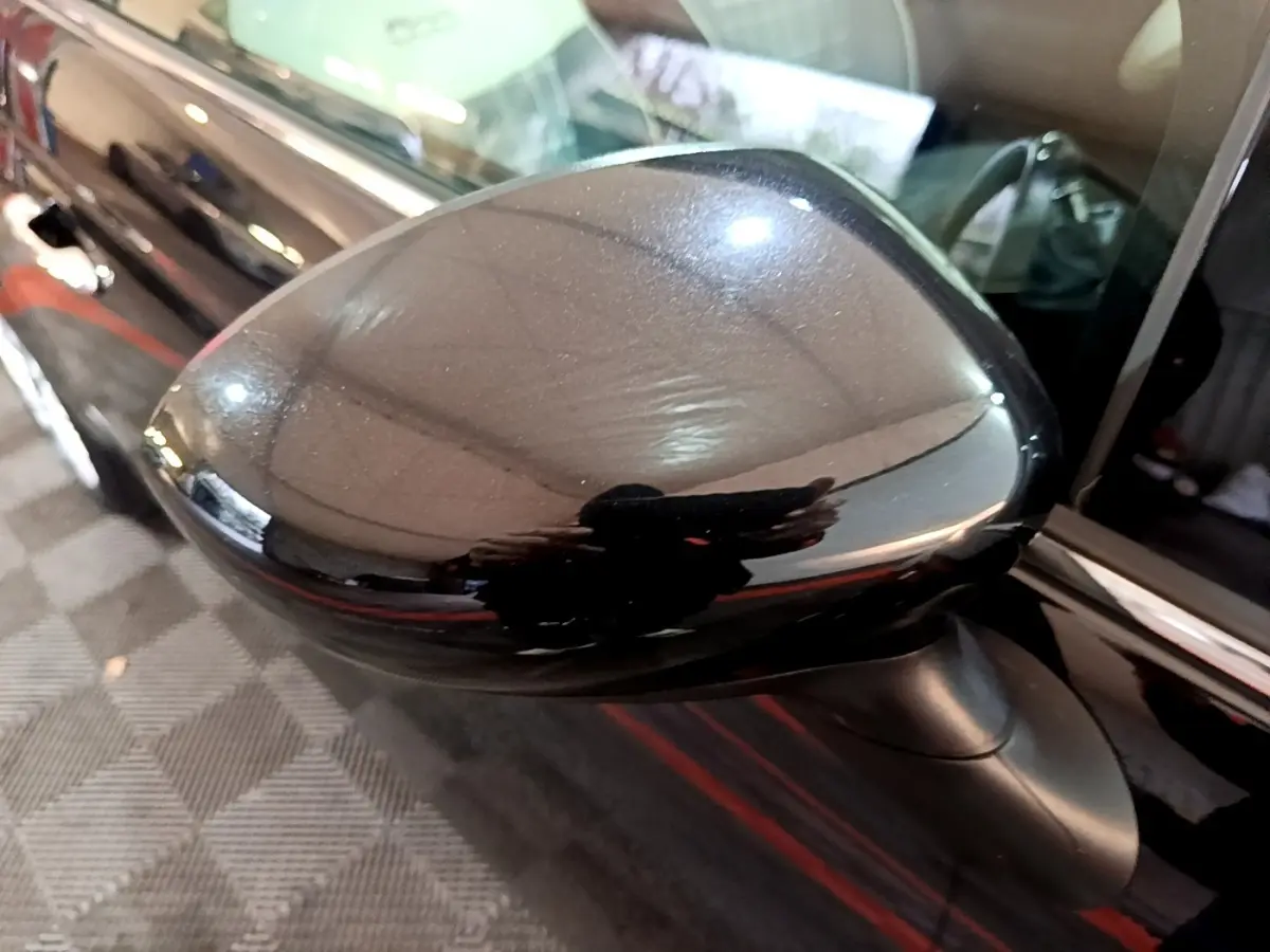 Gros plan sur le rétroviseur côté conducteur noir brillant de la Fiat 500 Lounge 2019, avec reflet de l'environnement intérieur.